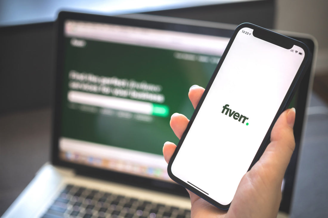 Macbook Pro with Fiverr.com homepage and a iPhone with hand howing Fiverr mobile app loading screen.